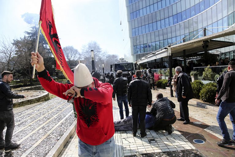 A protester holding an Albanian flag tries to escape from tear gas during an anti-government rally in Tirana, Albania, on Saturday, March 16, 2019. Albanian opposition supporters clashed with police while trying to storm the parliament building Saturday in a protest against the government which they accuse of being corrupt and linked to organized crime. (AP Photo/Visar Kryeziu)