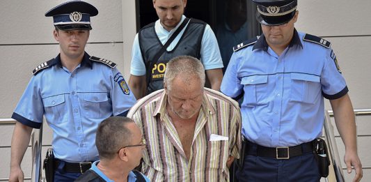 Police officers escort Gheorghe Dinca, the suspect in the case of rape and murder of a 15 year-old girl, from a court in Craiova, southern Romania, Saturday, July 27, 2019. Thousands of people took part Saturday evening in Bucharest in a march protesting the handling of the case, blaming Romanian officials for negligence, incompetence and a lack of empathy. (AP Photo/Bogdan Danescu)